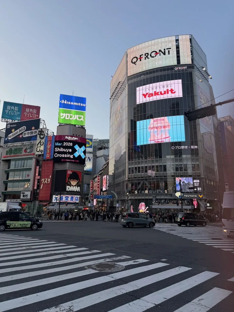 Shibuya Crossing at street level with big screens on the buildings, before sunset